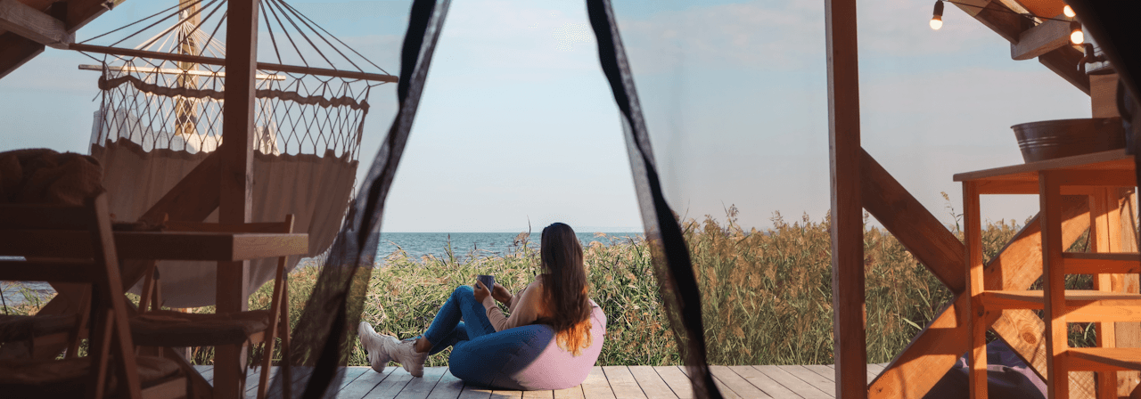 Eine Frau sitzt beim Camping auf der Veranda und blickt auf den See.