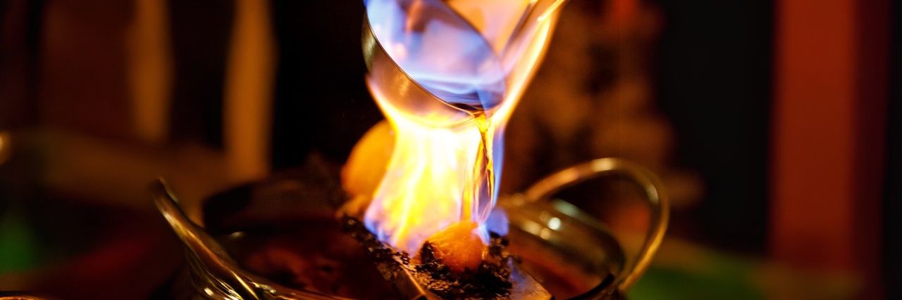 Brennender Zuckerhut über einer Feuerzangenbowle, Rum wird mit einer Kelle über die offene Flamme gegossen.